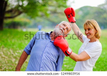 couple elderly fighting each other with boxing red gloves in park