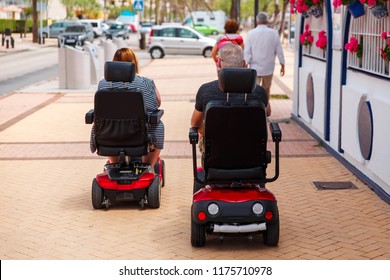 Couple elderly people ride along the sidewalk to an electric wheelchair. Motorized wheelchair. Mobile scooter. - Powered by Shutterstock