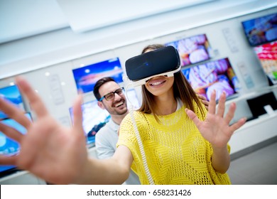 Couple in electronics store, exploring VR goggles.