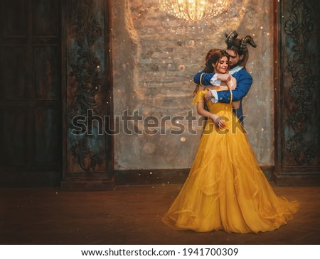 Couple embrace in room old castle. beauty and beast Happy woman fantasy princess in yellow dress guy is enchanted prince, horns on head. Romantic male hugs girl in arms. Man monster carnival costume