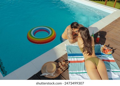 A couple embraces by the pool while kissing with a colorful inflatable ring nearby, under the summer sun - Powered by Shutterstock