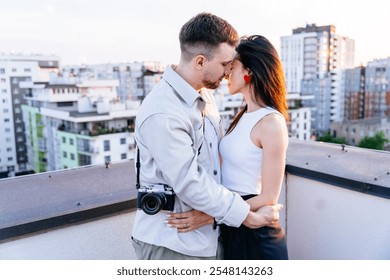 Couple embracing on city rooftop sun sets. Man with camera gently holds woman in affectionate moment modern buildings in background. Intimacy and romance concept. - Powered by Shutterstock