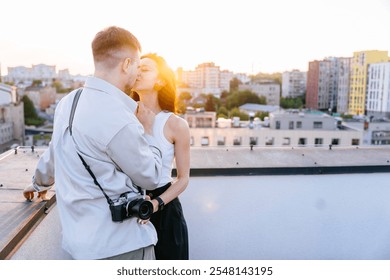 Couple embracing on rooftop with sunset city view. Man holding camera while gently kissing woman, love and connection. Adults expressing affection against vibrant cityscape. - Powered by Shutterstock