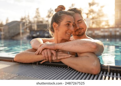 Couple embracing in a pool at sunset, woman smiling and leaning on man's shoulder in a Hotel. Spa, retreat, relaxation and Beauty and body care concept image  - Powered by Shutterstock