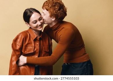 Couple embracing and smiling with affection in studio, young man kissing woman on cheek, warm clothing and casual style for love happiness and relationship.