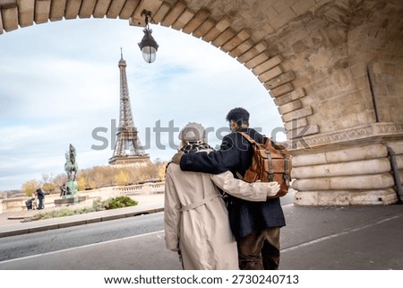 Couple embracing while walking under a stone arch bridge, enjoying a romantic travel sightseeing tour and admiring the iconic eiffel tower on a cloudy day in paris, france