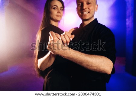 Couple engaged in a dance pose inside a studio, with colorful lighting creating a vibrant atmosphere, highlighting their handhold and close connection
