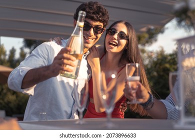 Couple of engaged young people pouring champagne into flute glasses celebrating their love - cheerful friends drinking sparkling wine smiling and having fun together
