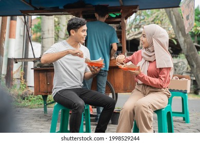 Couple Enjoy Eating Chicken Satay They Bought From Street Food Seller In Indonesia Sitting On A Plastic Chair