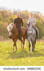 Couple enjoy riding horses in summer meadow.
