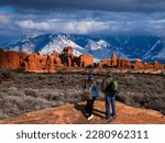 Couple enjoying beautiful mountain view on hiking trip in Utah. The Windows Section of the park, snow covered La Sal Mountains in the background.  Arches National Park ,Moab, Utah, USA.