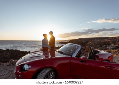 Couple enjoying beautiful views on the ocean, hugging together near the car on the rocky coast, wide view from the side with copy space on the sky - Powered by Shutterstock