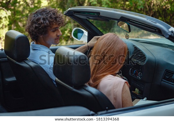 Couple enjoying a drive in a\
convertible in summer road. Friends going on holidays. Italian\
vacation serpentine roads, a redheaded woman and a beautiful young\
man