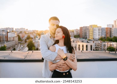 Couple enjoying peaceful moment on urban rooftop with city skyline in sunset light. Man gently hugs woman, relaxed and content. Love and tranquility, with wide city view. Connection on city backdrop. - Powered by Shutterstock