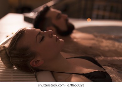Couple enjoying and relaxing in a jacuzzi bath with warm water, bubbles and candle light. Focus on the girl's nose and lips
