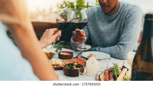 Couple Enjoying Romantic Dinner At Restaurant Terrace Drinking Red Wine And Eating Healthy Mediterranean Food, Lovely Couple Making Cheers With Red Wine Glasses At Summer Day At Terrace