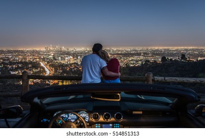 Couple enjoying skyline view from their car in the night. Focus on the Los angeles city in the background