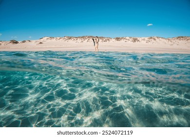 A couple enjoying a sunny day at a pristine beach with clear turquoise water and sandy dunes in the background.. - Powered by Shutterstock