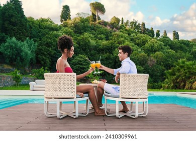 Couple enjoying a sunny day with a toast by a luxurious pool, surrounded by lush greenery. - Powered by Shutterstock