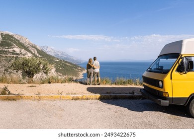 Couple enjoying the view of Croatian mountainous coast standing by their retro yellow camper van parked on a cliff, Croatia - Powered by Shutterstock