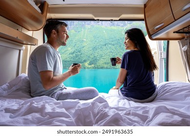 A couple enjoys coffee and a scenic view of a Norwegian fjord from the bed of their campervan. a diverse couple of men and women a t a mobile home in Lovatnet Lake Lodal valley Norway - Powered by Shutterstock