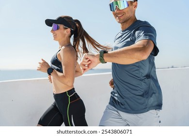 A Couple Enjoys a Morning Jog Along a Sunny Waterfront Promenade While Wearing Fitness Trackers - Powered by Shutterstock