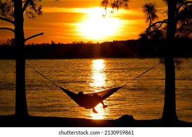 A Couple Enjoys The Sunset Above The Mississippi River From A Hammock In New Orleans Audubon Park