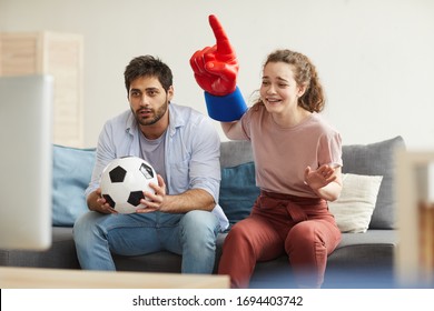 Couple of enthusiastic sport fans watching football match on TV at home and cheering emotionally, focus on young woman wearing foam finger, copy space - Powered by Shutterstock