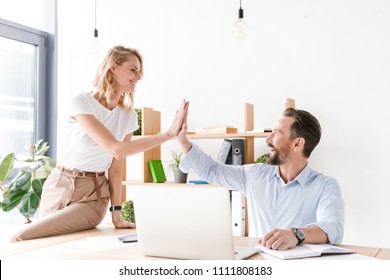 Couple Of Excited Colleagues Giving High Five While Sitting At The Office