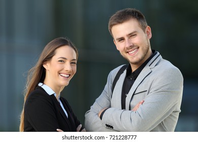 Couple of executives posing looking at camera standing on the street with an office building in the background