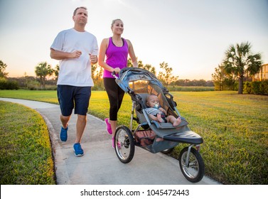 Couple Exercising And Jogging Together At The Park Pushing Their Baby In A Stroller