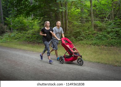 Couple Exercising And Jogging Together Pushing Their Baby In A Stroller