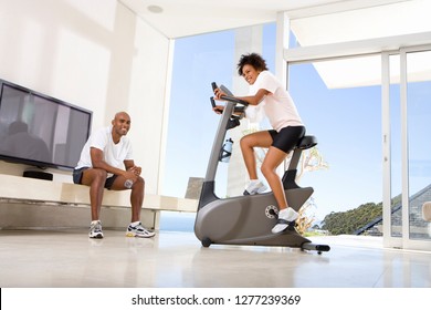 Couple Exercising On Gym Equipment And Bike At Home Together