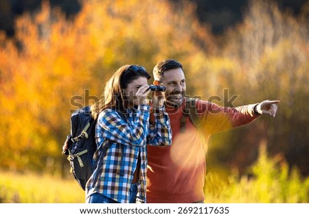 A couple experiences nature together while birdwatching, surrounded by colorful autumn foliage, with one partner using binoculars.