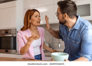 couple experiences tension while having breakfast in their kitchen. The woman, looking frustrated, tries to explain her point, while the man raises his hand in defiance, avoiding the conversation.