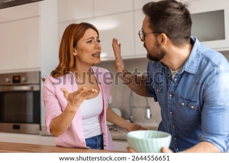 couple experiences tension while having breakfast in their kitchen. The woman, looking frustrated, tries to explain her point, while the man raises his hand in defiance, avoiding the conversation.