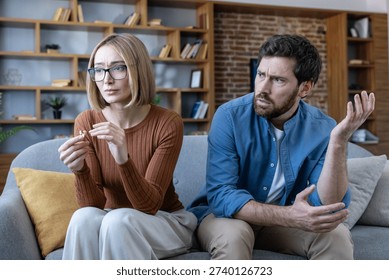 Couple experiencing relationship problems at home, a sad woman holding a divorce ring while an upset man is arguing, symbolizing breakup and marital issues
