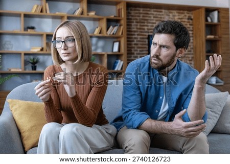 Couple experiencing relationship problems at home, a sad woman holding a divorce ring while an upset man is arguing, symbolizing breakup and marital issues
