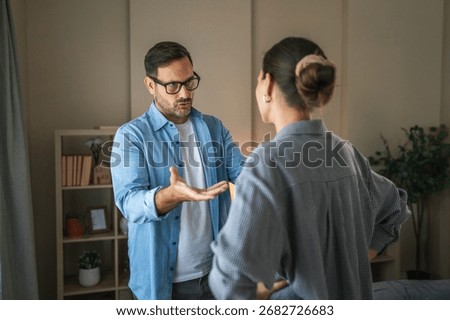 Couple experiencing relationship problems, man actively expressing frustration while woman turns away, representing a disagreement and tension within their cohabiting space