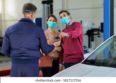 Couple With Face Mask Giving Keys Of Their Car To Auto Repairman In A Workshop. 