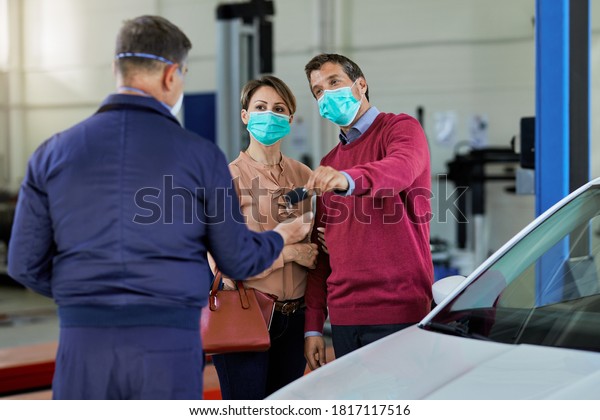 Couple with face mask giving keys of their car\
to auto repairman in a workshop.\
