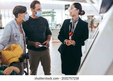 Couple In Face Masks Standing With Airport Staff Wearing Face Shield. Ground Staff Assisting Tourist Family At Airport In Pandemic.