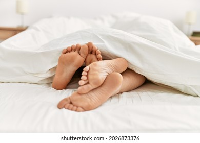 Couple feet under sheets on the bed at home.