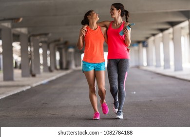 Couple of female friends jogging on the city street under the city road overpass.They relaxing after jogging and making fun.Embracing each other. - Powered by Shutterstock