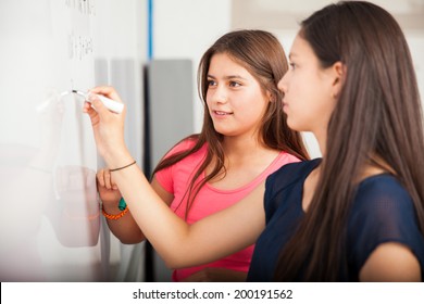 Couple Of Female High School Students Writing On A White Board During Class