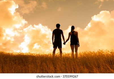 Couple in a field holding hands and watching sunset