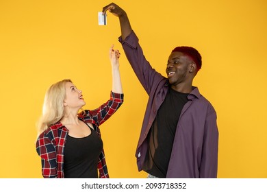 Couple Finances. Family Income. Shopping Together. Happy Multiracial Millennials  Man Teasing Money Greedy Shopaholic Woman With Credit Card Isolated On Orange Background.