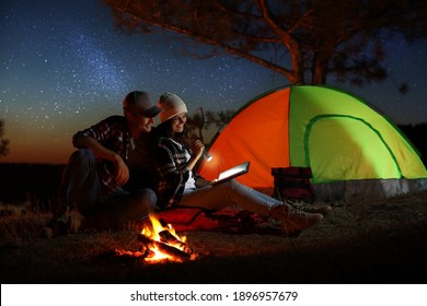 Couple with flashlight reading book near bonfire at night. Camping season - Powered by Shutterstock