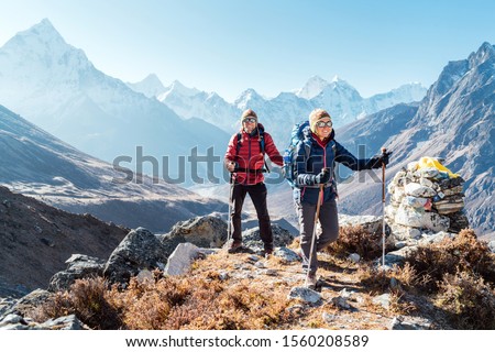Couple following Everest Base Camp trekking route near Dughla 4620m. Backpackers carrying Backpacks and using trekking poles and enjoying valley view with Ama Dablam 6812m peak