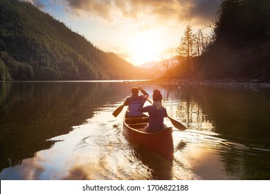 Couple friends canoeing on a wooden canoe during a colorful sunny sunset. Cloudy Sky Composite. Taken in Harrison River, East of Vancouver, British Columbia, Canada. - Powered by Shutterstock